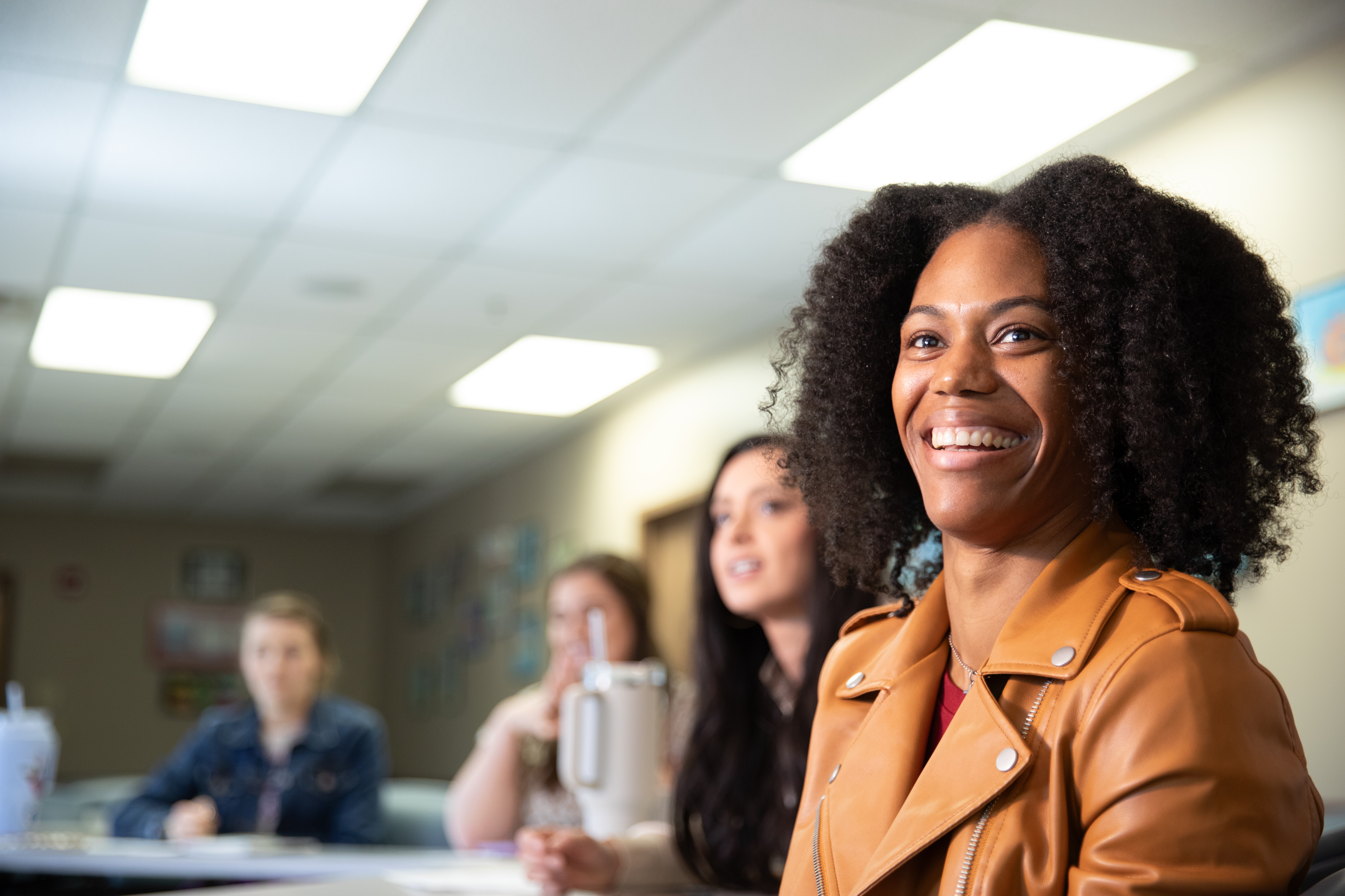 Health Promotion and Wellness alumna Terri Roberts is pictured in a tan leather jacket seated at a conference table.