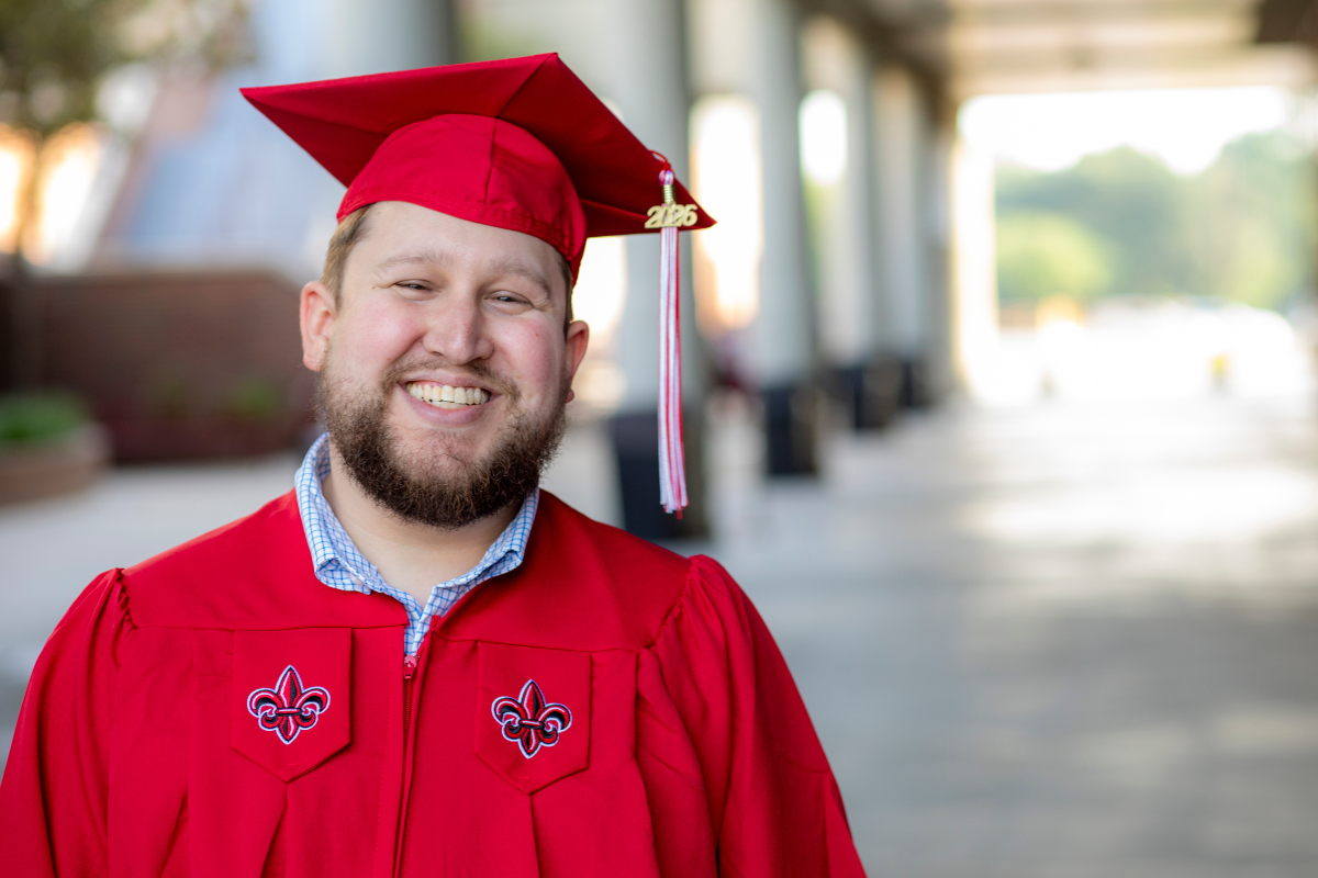 Jace Nugier smiles for a portrait in his red UL Lafayette mortarboard cap and gown.
