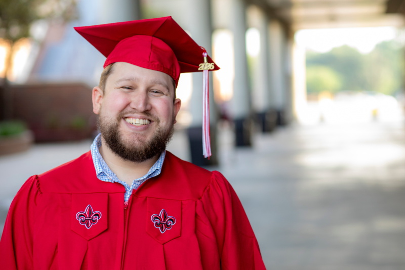 Jace Nugier smiles for a portrait in his red UL Lafayette mortarboard cap and gown.